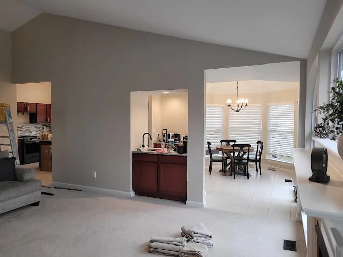 This is an image from SNL Painting Inc, located in Missouri. The image shows a freshly painted interior living space with soft gray walls, white trim, open doorways, and adjacent kitchen and dining areas, highlighting professional interior painting and wall finishing services.