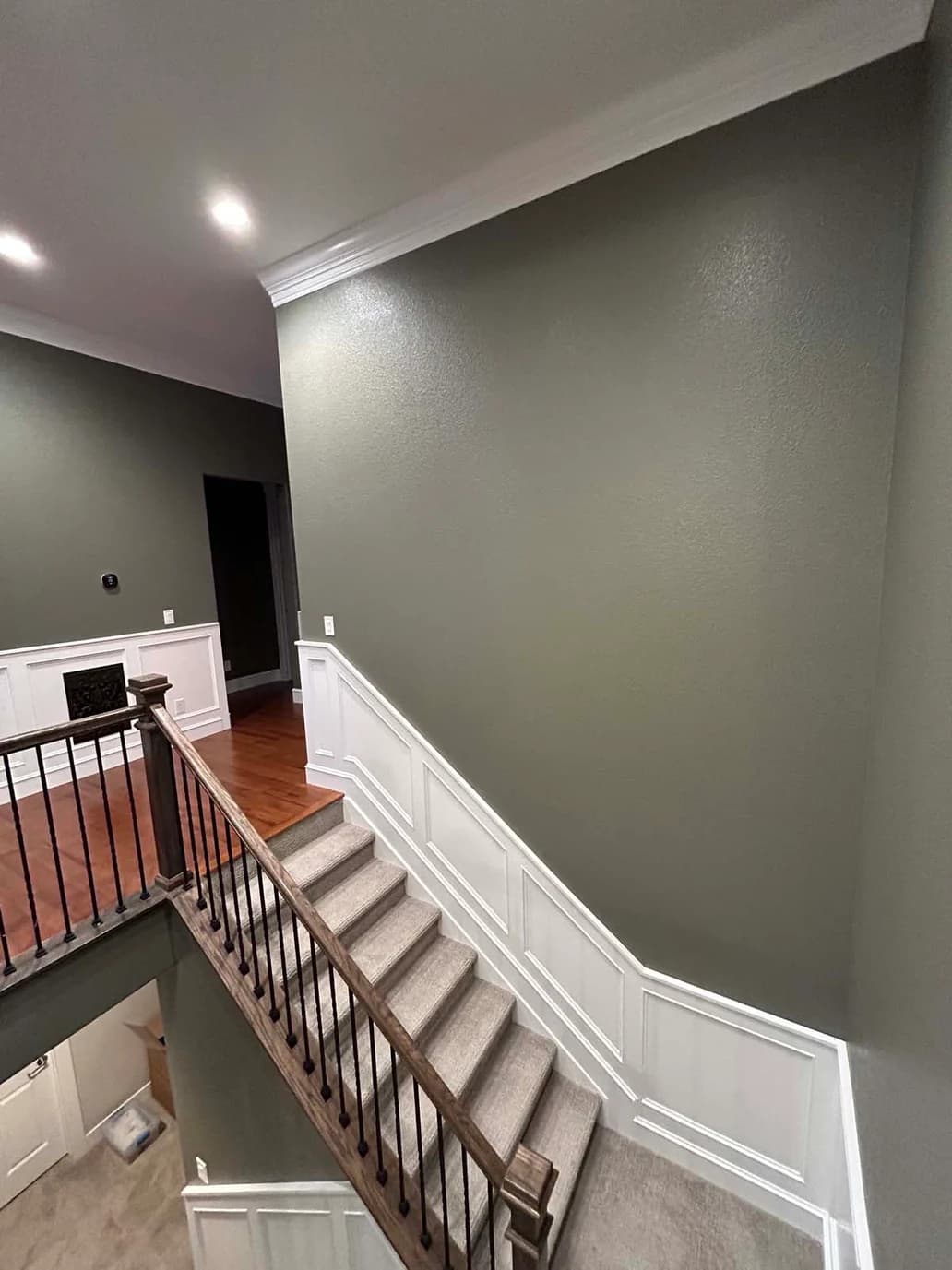 This is an image from Fresh Coat Painters of Wichita.The image shows a newly painted interior stairway featuring smooth olive-green walls paired with bright white wainscoting and crown molding. The fresh paint highlights the updated trim work and creates a clean contrast along the staircase.