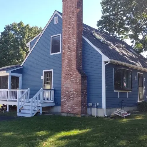 This is an image from Promark Painting, located in Massachusetts. It features a blue painted home with a brick chimney, white trim, and a light gray deck, giving the property a polished, updated look.