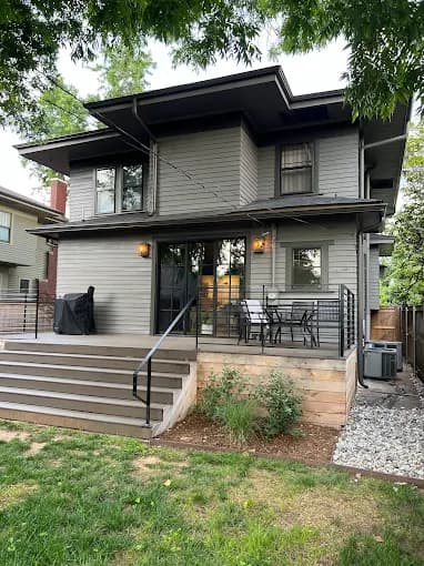 This is an image from Fixable Painting, located in Oklahoma City, Oklahoma. The photo shows the back view of a gray-painted house with a raised wooden deck, black railings, and an outdoor dining space.