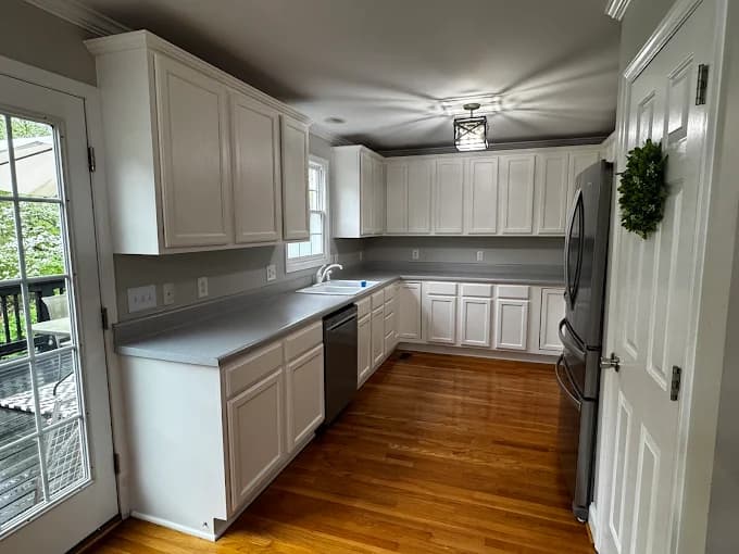 Cabinet painting project by Triangle Pro Painting in Raleigh, NC. The image shows a kitchen with white cabinets, gray backsplash, and wood flooring.