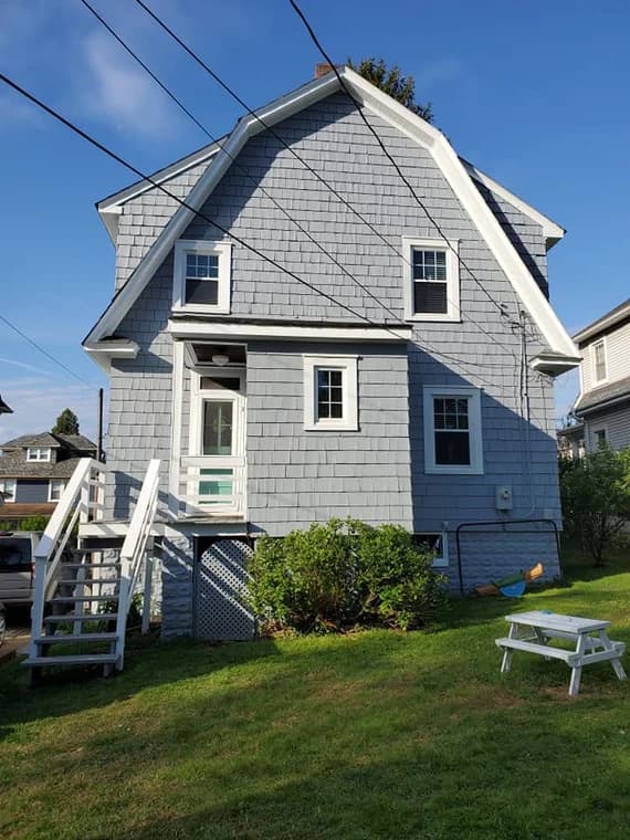 This is an image from Hands On Painters, located in Maryland. The picture shows the back of a gray-shingled house with white trim, outdoor stairs, and a grassy yard.