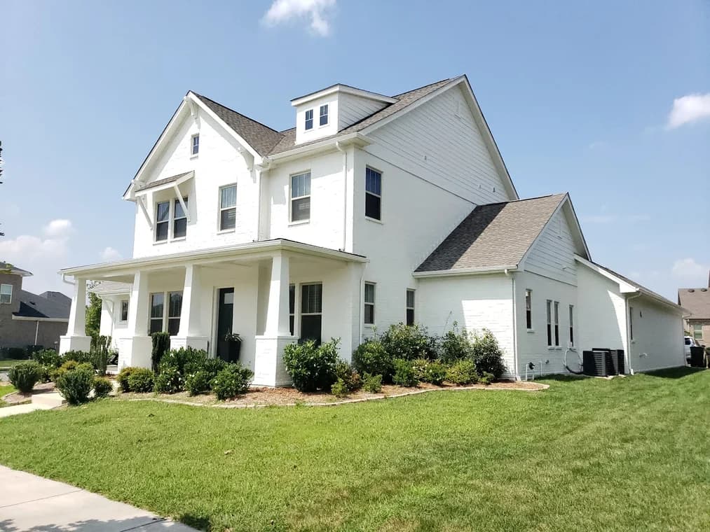 Exterior painting project by Paint EZ of Charlotte in Charlotte, NC. The image shows a white two-story home with black shutters, porch columns, and shrubs.
