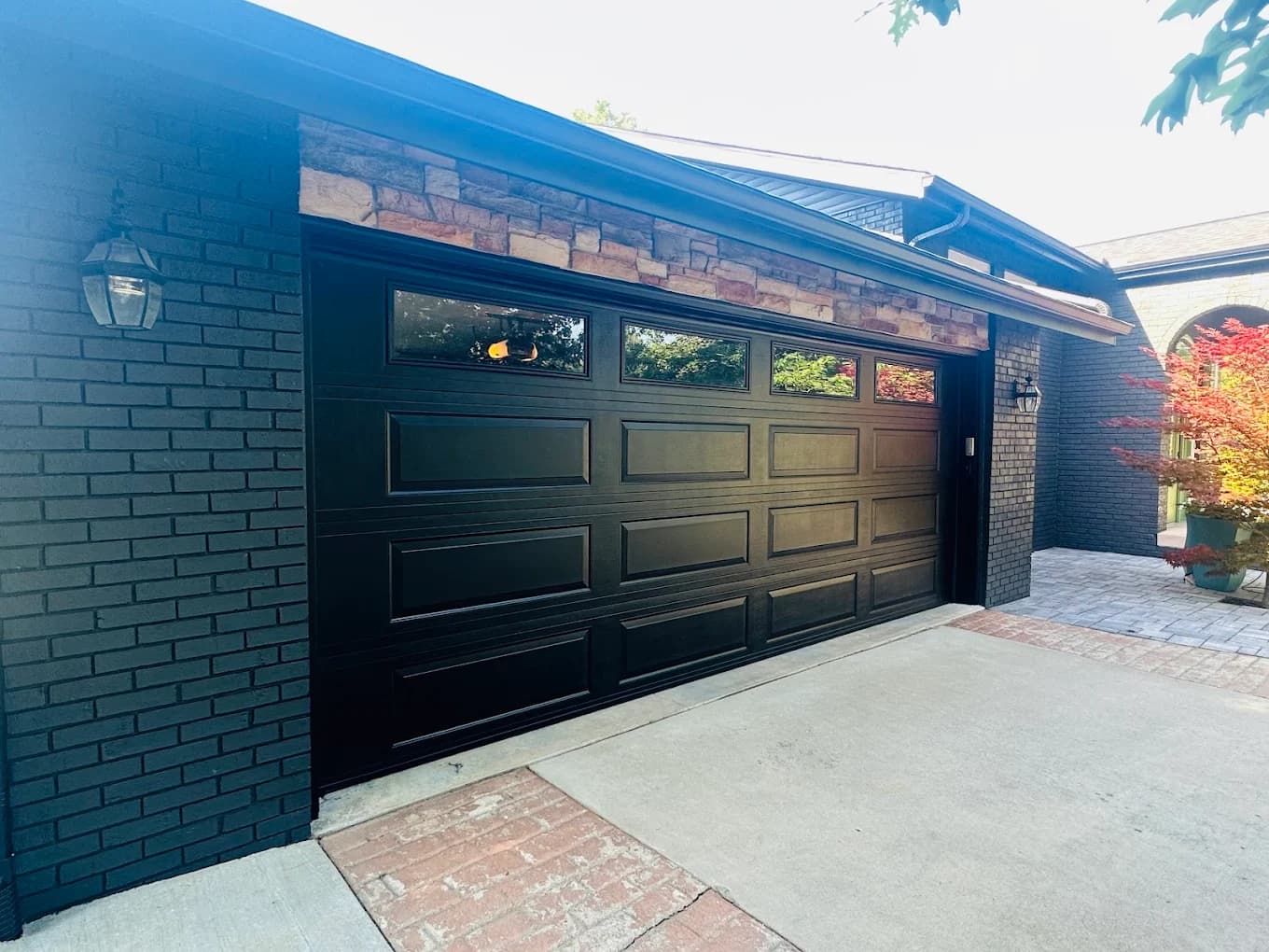 Exterior painting project by Cinric Painting in Pawnee, Illinois. The image shows a black garage door, painted brick, and stone accents beside a driveway.