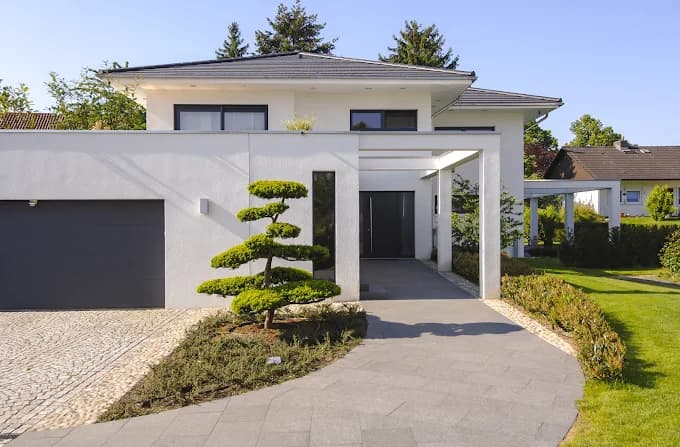 This is an image from Five Star Painting, showing a contemporary home with light-colored painted walls and dark roofing. The crisp white exterior highlights the landscaped garden and modern architectural details.