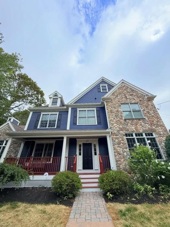 A two-story home with navy blue siding, stone accents, and a red porch, professionally painted to enhance curb appeal.