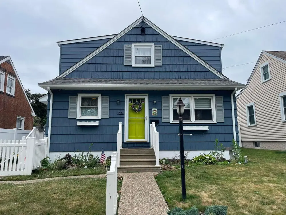 Exterior of a blue two-story home with a bright green front door, freshly painted siding, and gray shutters, showcasing residential painting work by Painting Plus Home Improvement LLC.