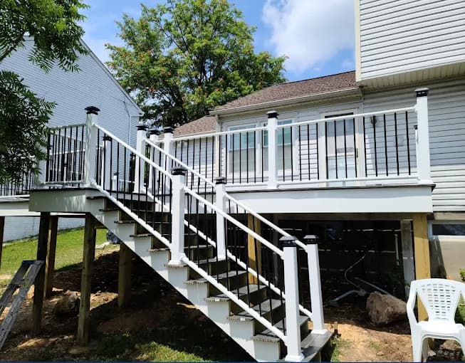 This is an image from Julio's Painting LLC, located in Maryland. The image displays a raised outdoor deck with white railings, black balusters, and a newly finished staircase leading to the yard.