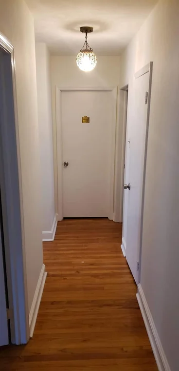 This is an image from All in the Family Painting company, located in Brookhaven, PA. The image is a freshly painted residential hallway with white walls, wood flooring, and updated trim work. 