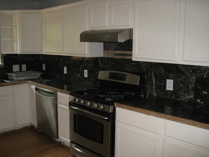 This is an image from Next Door Painting, located in Texas. The kitchen shows white repainted cabinets paired with dark marble countertops and stainless steel appliances.