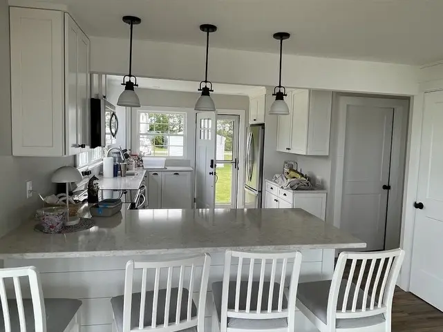 This is an image from R&R Painting & Concrete Coatings, located in New York. The interior kitchen features white cabinetry, a large island with seating, pendant lights, and updated finishes.