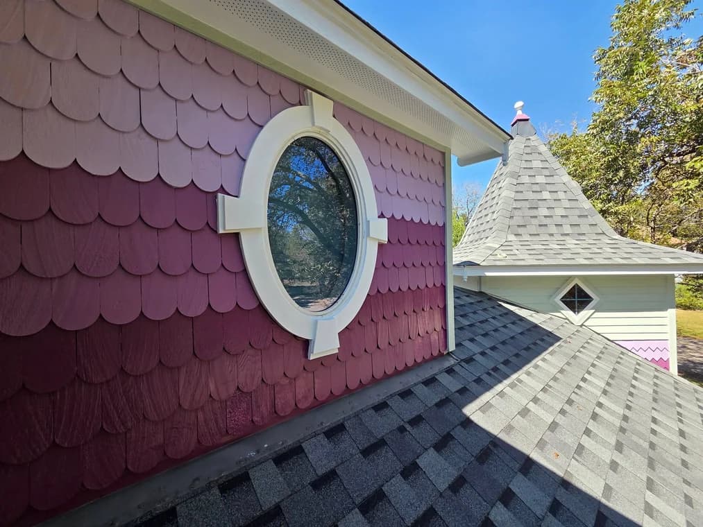 "This is an image from Reyes Painting Co., located in Texas. The photo shows a close-up of a painted exterior wall with scalloped siding in shades of mauve and purple beside a gray shingled roof."