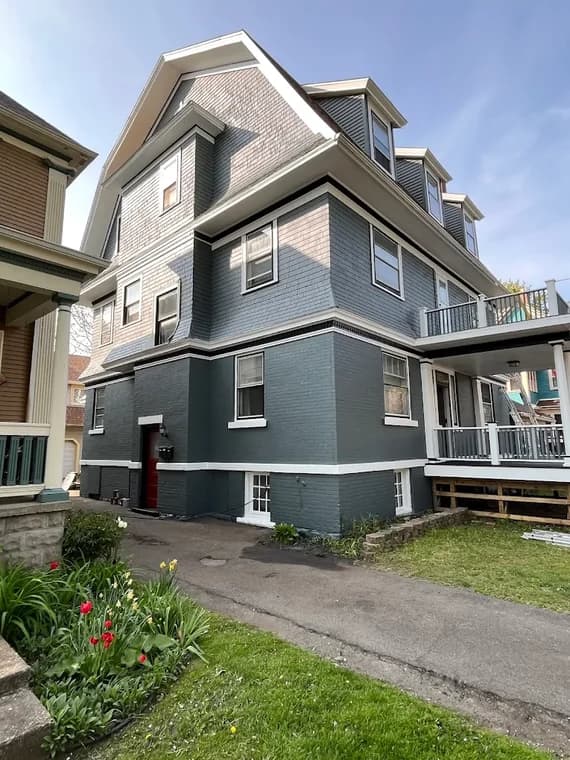 This is an image from Northeast Pro Painting & Restoration, located in New York. The photo shows a large multi-story home with freshly painted blue-gray siding and white trim, highlighting clean lines and detailed exterior restoration work.