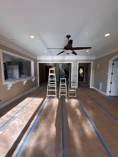 Interior painting project by GW Painting in Charlotte, NC. The image shows a room with gray walls, wood floors, a ceiling fan, and painter tape.