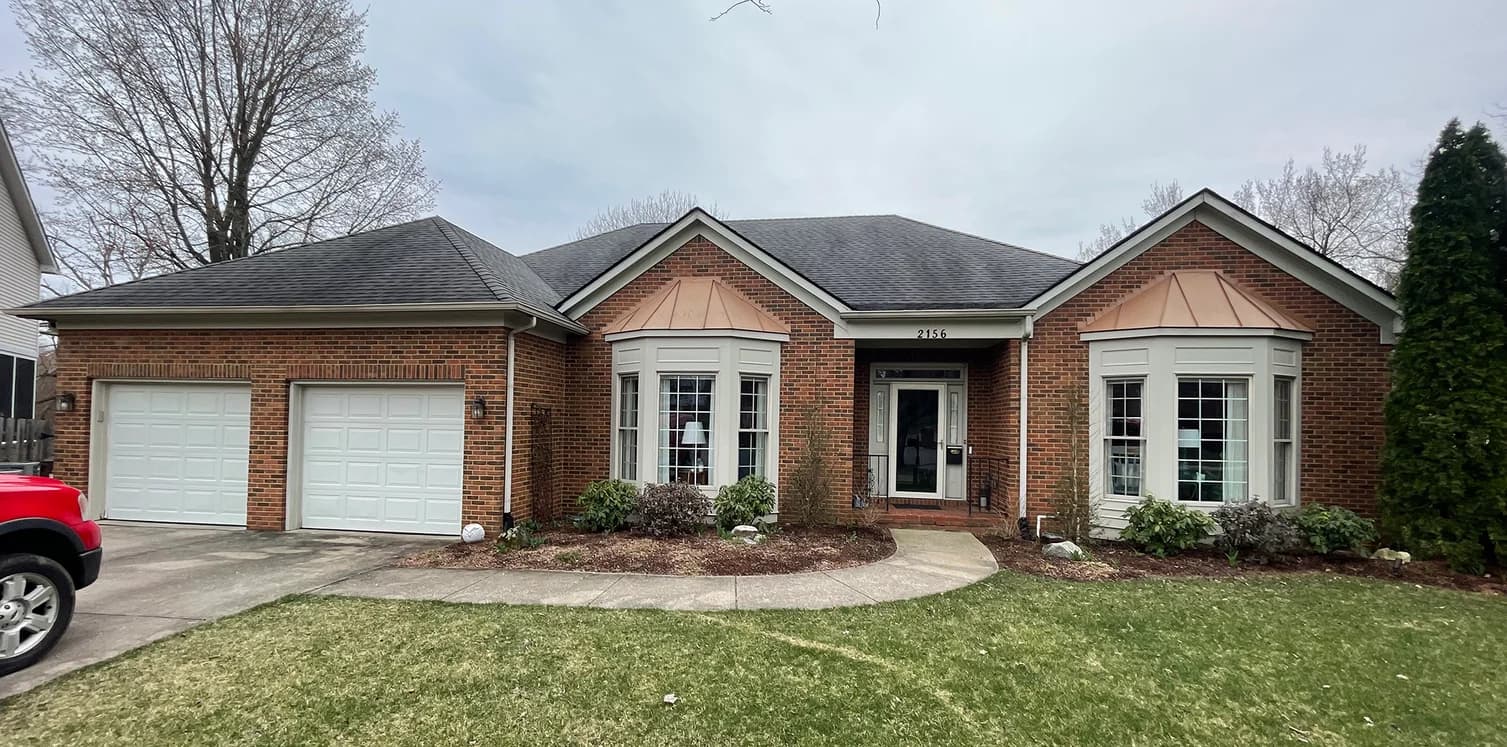 This is an image from Big J Painting LLC, located in Kentucky. The photo shows a single-story brick home with white trim and copper roof accents freshly painted, showcasing exterior residential painting work.