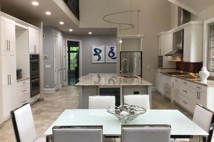 Cabinet painting project by Fulton Revivals in Chicago, IL. The image shows a bright white kitchen with an island, dining table, and recessed lights.