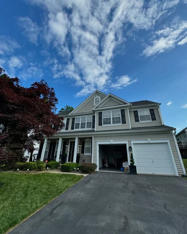 This is an image from Santana Painting Co, located in Maryland. The photo shows a two-story suburban home with beige siding, black shutters, and a well-kept front yard under a bright blue sky.