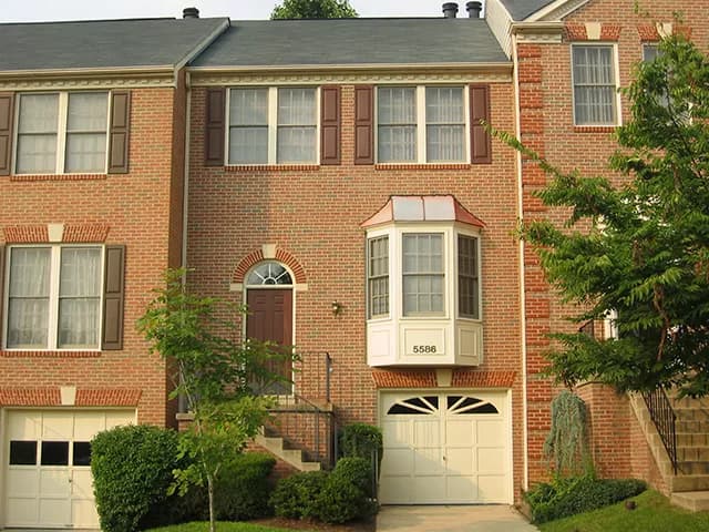 This is an image from Donovan’s Painting, located in Maryland. The picture shows a brick townhouse with cream trim, maroon shutters, and a neatly maintained exterior.