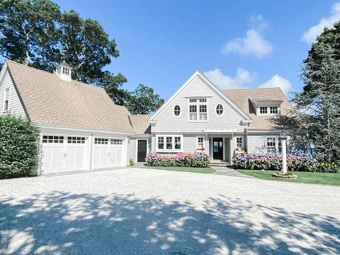 This is an image from Stewart Painting, located in Massachusetts. The photo shows the exterior of a large home with freshly painted light gray siding, white trim, and landscaped flower beds.