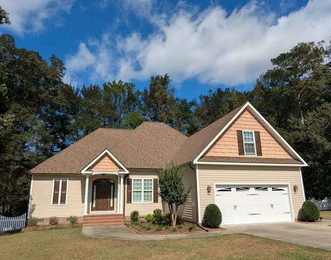 Exterior painting project by CertaPro Painters of Clayton-Greenville, NC in Clayton, NC. The image shows a beige one-story home with garage and blue sky.