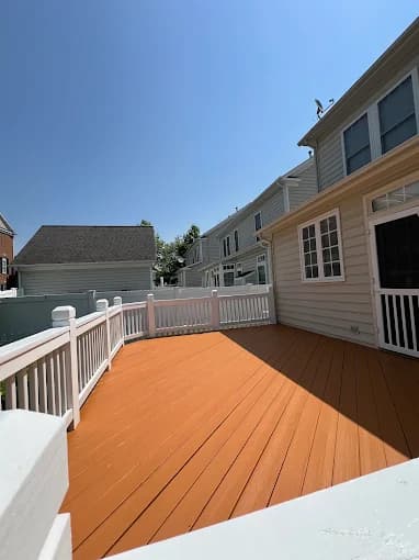 This is an image from C&R Pro Painting, located in Virginia. The picture shows a newly stained outdoor deck with a warm wood-tone finish and white railing under clear blue skies.