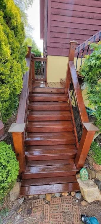 Deck staining project by Diaz Professional Painting in Burnsville, NC. The image shows glossy wood stairs, railings, and red exterior siding.