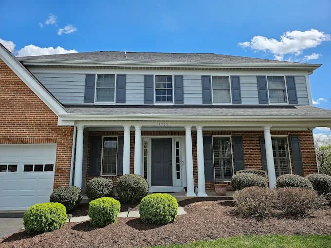 This is an image from C&R Pro Painting, located in Virginia. The exterior photo shows a two-story home with freshly painted gray siding, dark shutters, white trim, and brick accents.