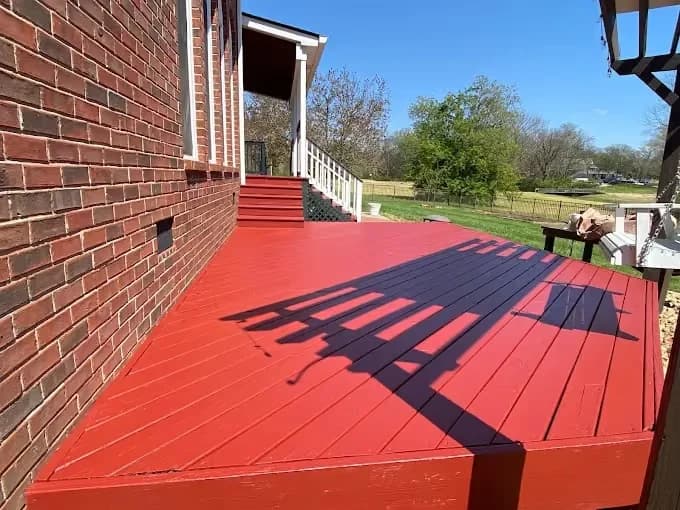 Painting project by New Direction Painting in Franklin, Tennessee. The image shows a red-painted deck beside a brick home.