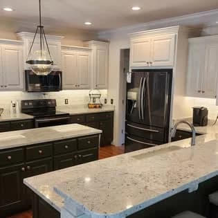 Cabinet painting project by Triangle Painting And Drywall llc in Raleigh, NC. The image shows white cabinets, dark base cabinets, a marble island, refrigerator, and pendant lights.