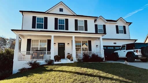 Painting project by Good Faith Painting Company in Knoxville, Tennessee. The image shows a white two-story home with black shutters and a covered porch.