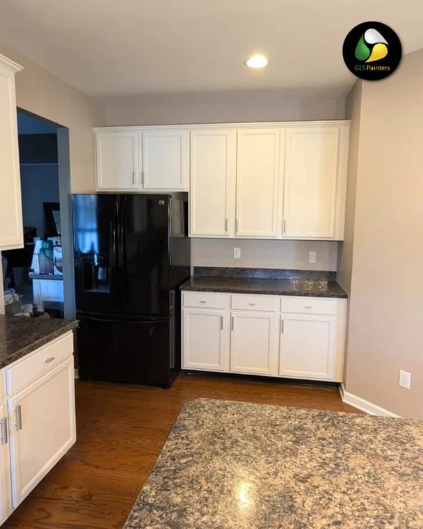 A modern kitchen with white cabinets, granite countertops, and a black refrigerator, showing the clean interior painting work by GLS Painters.