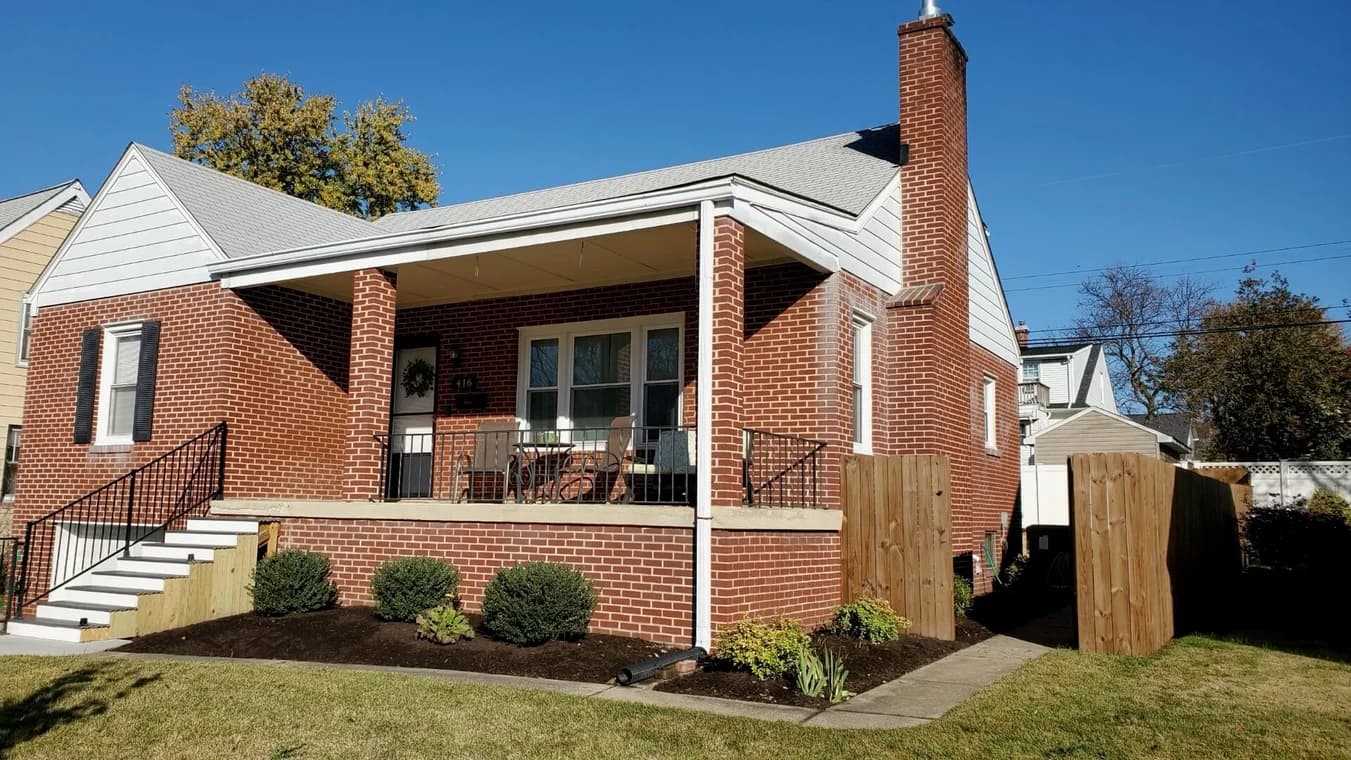 This is an image from Annapolis Coatings, located in Maryland. The picture shows a brick home with a freshly painted porch area, including white trim, black railings, and well-maintained landscaping.