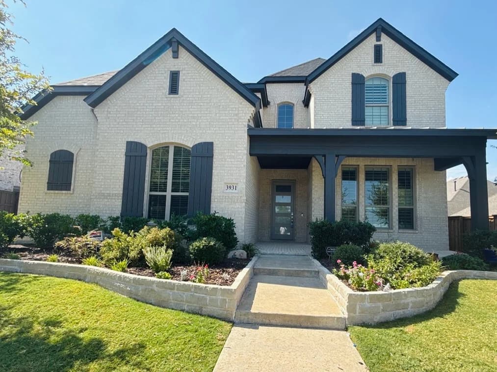 This is an image from Spray Tex Painting, located in Texas. The outdoor photo shows a two-story brick home with dark shutters, a covered entryway, and well-maintained landscaping.