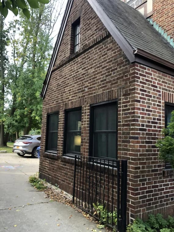 This is an image from Northeast Pro Painting & Restoration, located in New York. The photo shows a brick home with newly painted black window trim, creating a modern contrast against the red brick exterior.