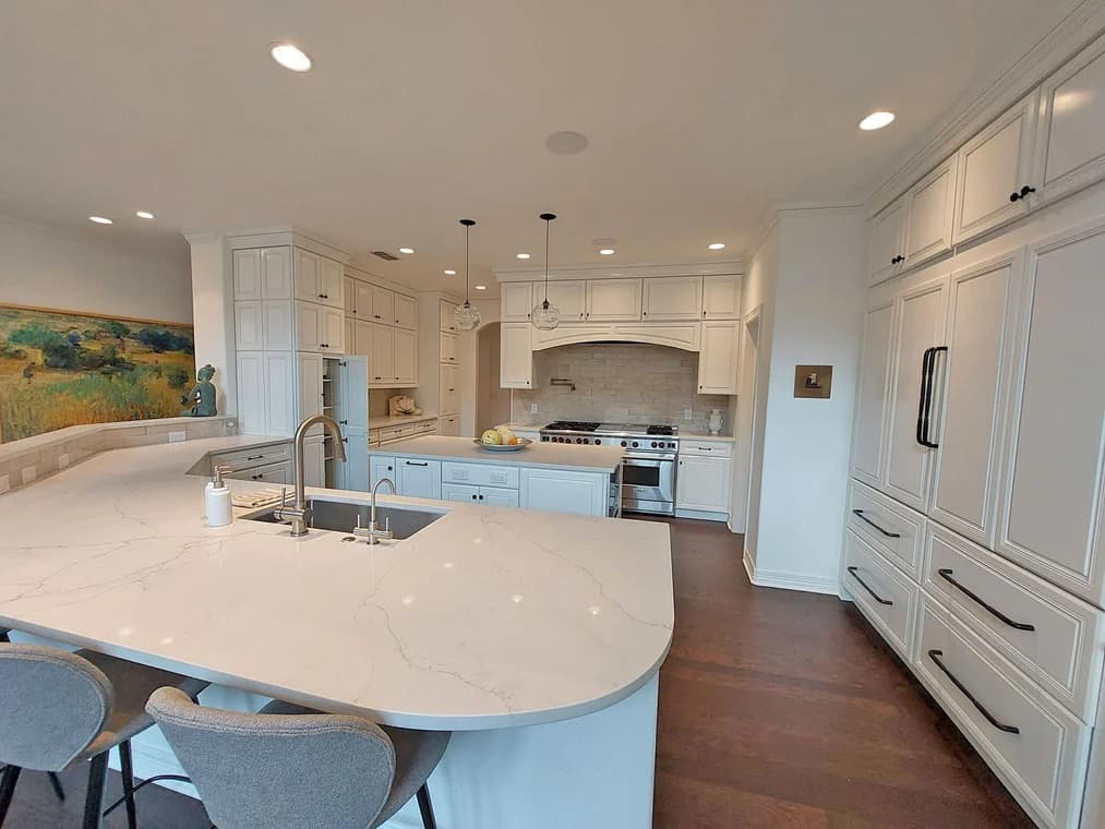 "This is an image from Paramo Painting, located in Texas. The kitchen shows white cabinetry, a large island with a marble-style countertop, pendant lighting, and stainless-steel appliances."