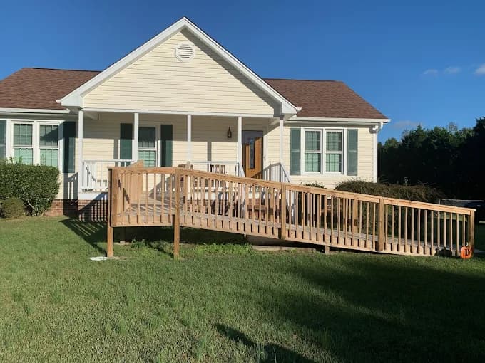 Exterior painting project by NC Paint & PowerWash in Garner, North Carolina. The image shows a beige home with green shutters, a white porch, and a wood ramp.
