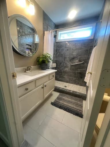This is an image from C & V Painting Services LLC, located in Virginia. The interior photo shows a remodeled bathroom with a walk-in tiled shower, white vanity, round mirror, and overhead lighting.