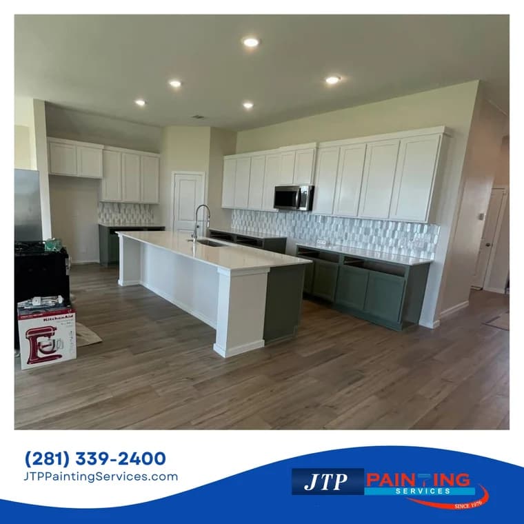 This is an image from JTP Painting Services, located in Texas. The picture shows a modern kitchen with a large island, white upper cabinets, green lower cabinets, and a decorative backsplash.