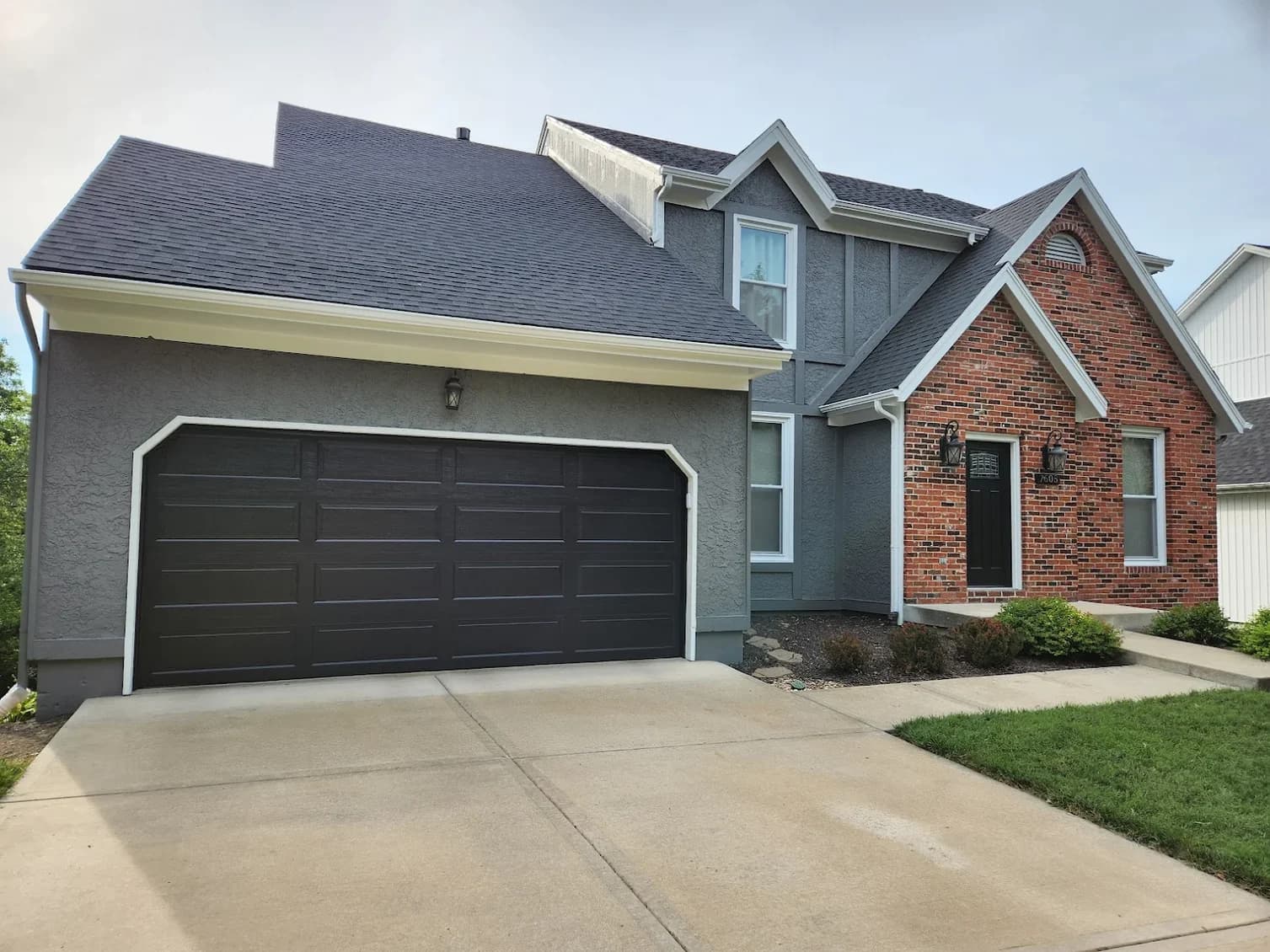 This is an image from Home Pros Painting And Home Repairs. The image shows a freshly painted two-story home featuring a smooth gray exterior finish, crisp white trim, and a bold black garage door, highlighting the updated curb appeal and clean exterior paintwork.