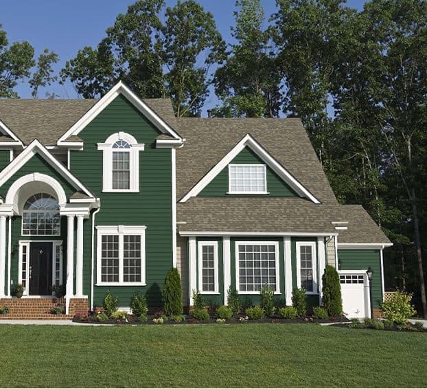 This is an image from JAT Painters Inc, located in New York. The exterior photo shows a green two-story home with white trim and tan roofing, highlighting a freshly painted façade with decorative windows.