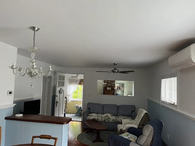 This is an image from CertaPro Painters of Cape Cod, located in Massachusetts. The photo shows a freshly painted living room with white upper walls, light blue lower walls, and a clean ceiling finish, creating a bright and inviting space.