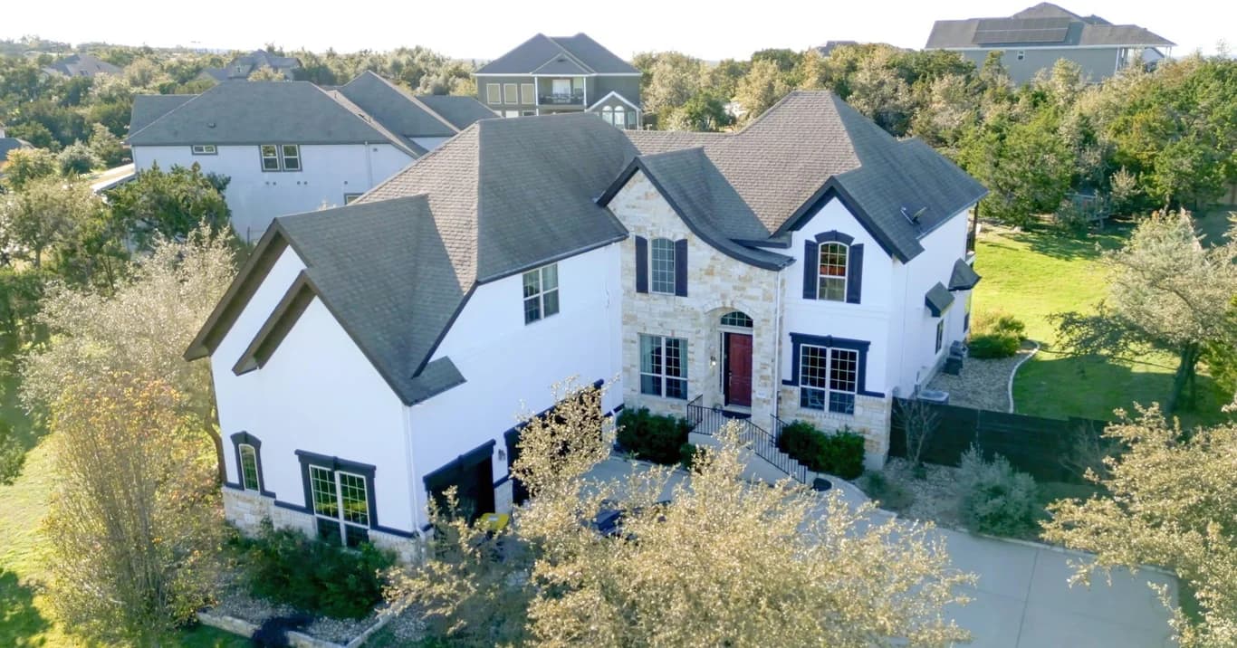 This is an image from That 1 Painter Greater Boston, located in Massachusetts. The photo shows a large residential home with a white and stone exterior, freshly painted trim, and a well-maintained yard.