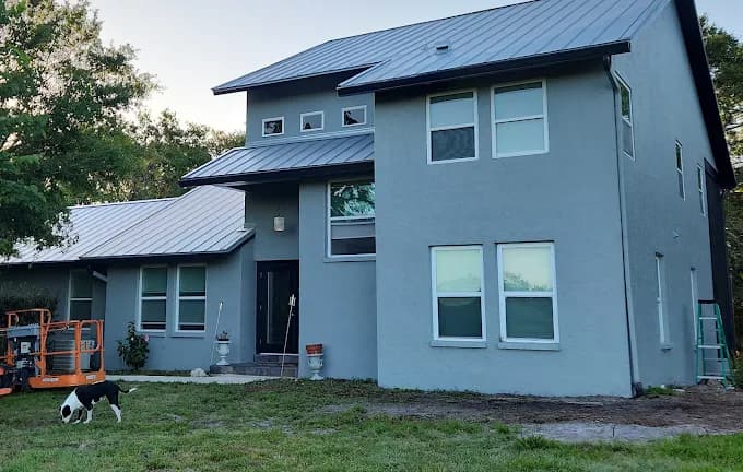This is an image from Paint Masters Painting Contractors LLC company, located in Venice, FL. The image is a modern two-story home with fresh gray exterior paint and black trim completed by Paint Masters Painting Contractors LLC