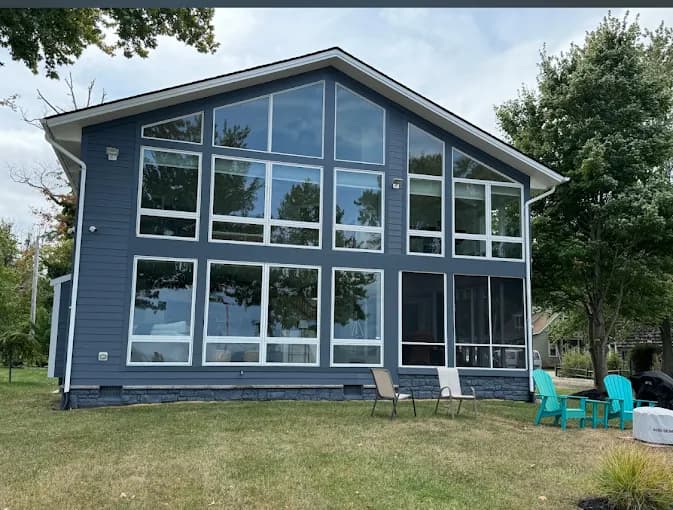 This is an image from Julio's Painting LLC, located in Maryland. The photo shows a large modern home exterior with expansive floor-to-ceiling windows and freshly painted blue siding.