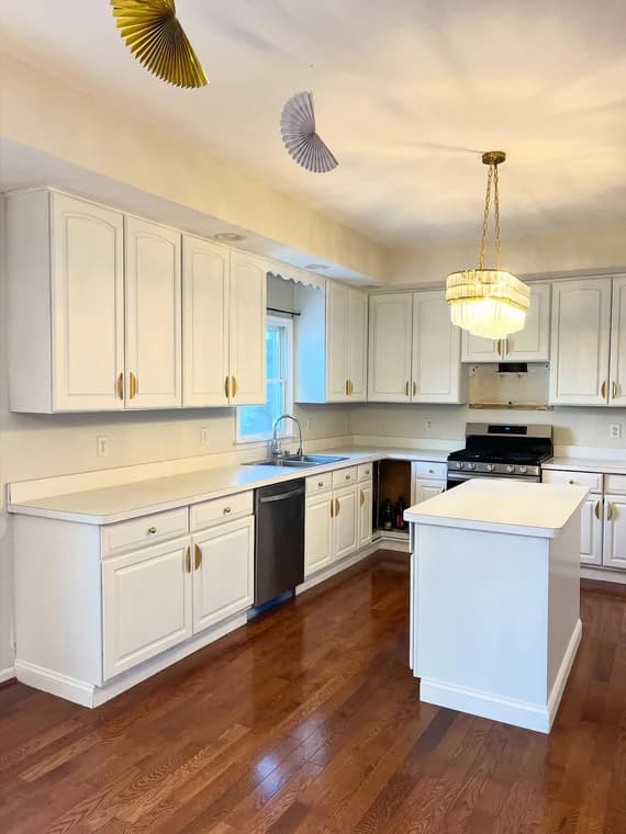 This is an image from Aurora Painting, located in Pennsylvania. The photo shows a bright kitchen with white cabinets, gold hardware, hardwood floors, and a modern chandelier above the island.