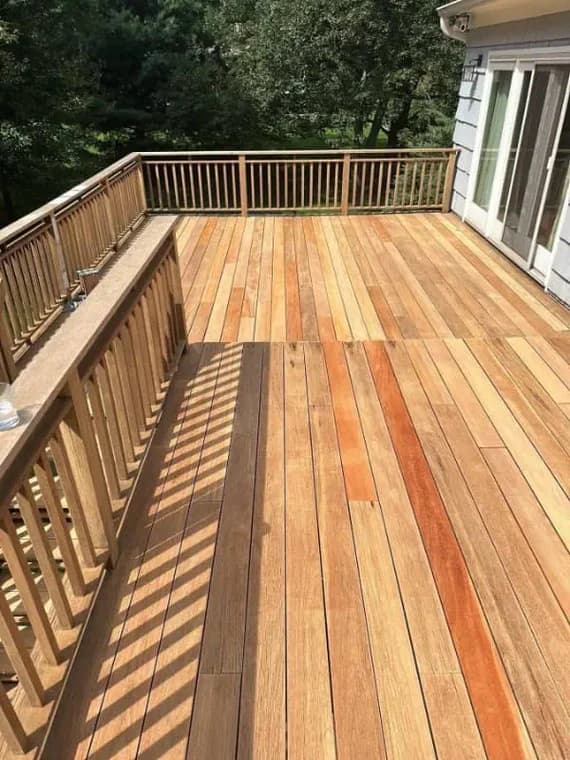 This is an image from Pier Painting Services, located in NY. The deck features freshly refinished wood planks and railings overlooking a wooded backyard.