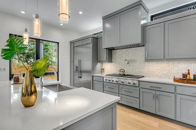 This is an image from EchoHousePainting, located in Massachusetts. The photo shows a modern kitchen with freshly painted gray cabinets, white quartz countertops, stainless steel appliances, and elegant pendant lighting.