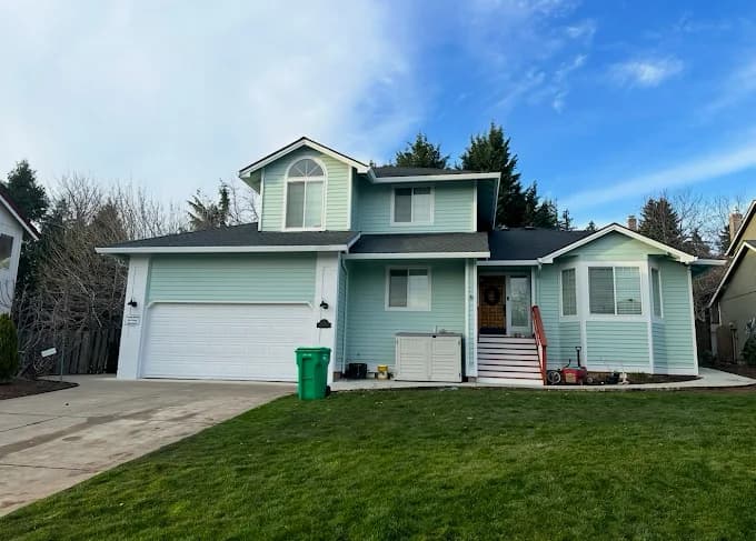 This is an image from Muir Painting Inc  company, located inHappy Valley, OR The image is a light blue two-story house with white trim and garage freshly painted by Muir Painting Inc exterior house painting contractors
