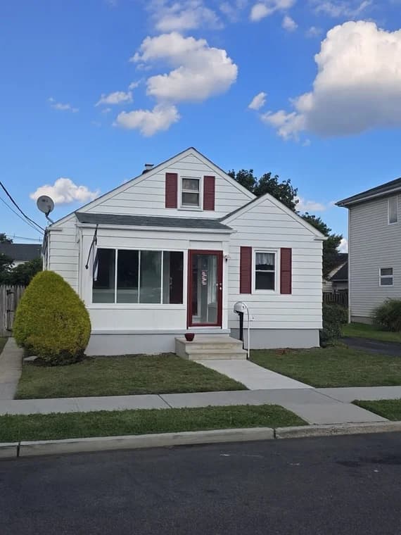 This is an image from That 1 Painter North Jersey. It displays the front of a small white house with red shutters and a red front door, recently painted for curb appeal.