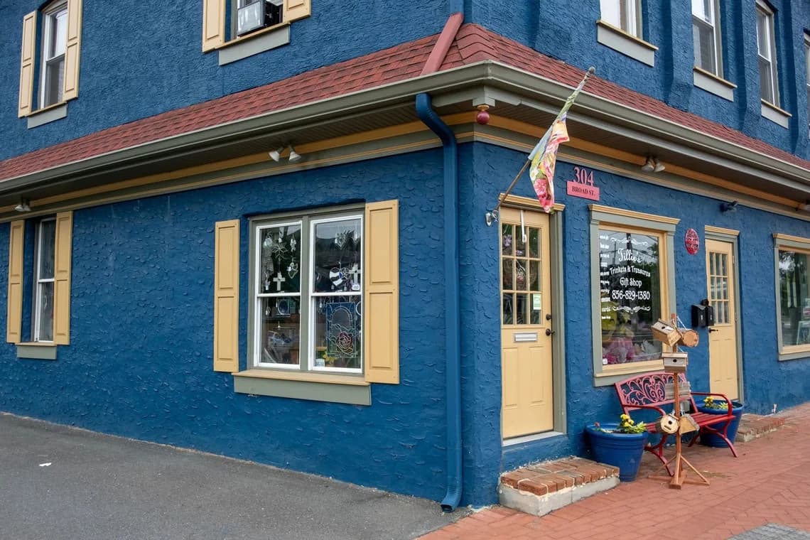 A blue commercial storefront with beige trim and shutters, featuring a bright red roof and flag outside.